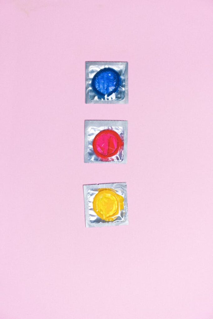 Top view arrangement of multicolored latex condoms composed in row on light pink surface